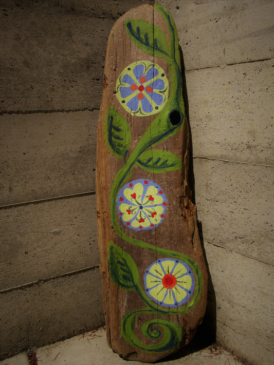 Folk art flowers painted on driftwood by Lone Peep: a green vine with three round blue, yellow and red blooms.