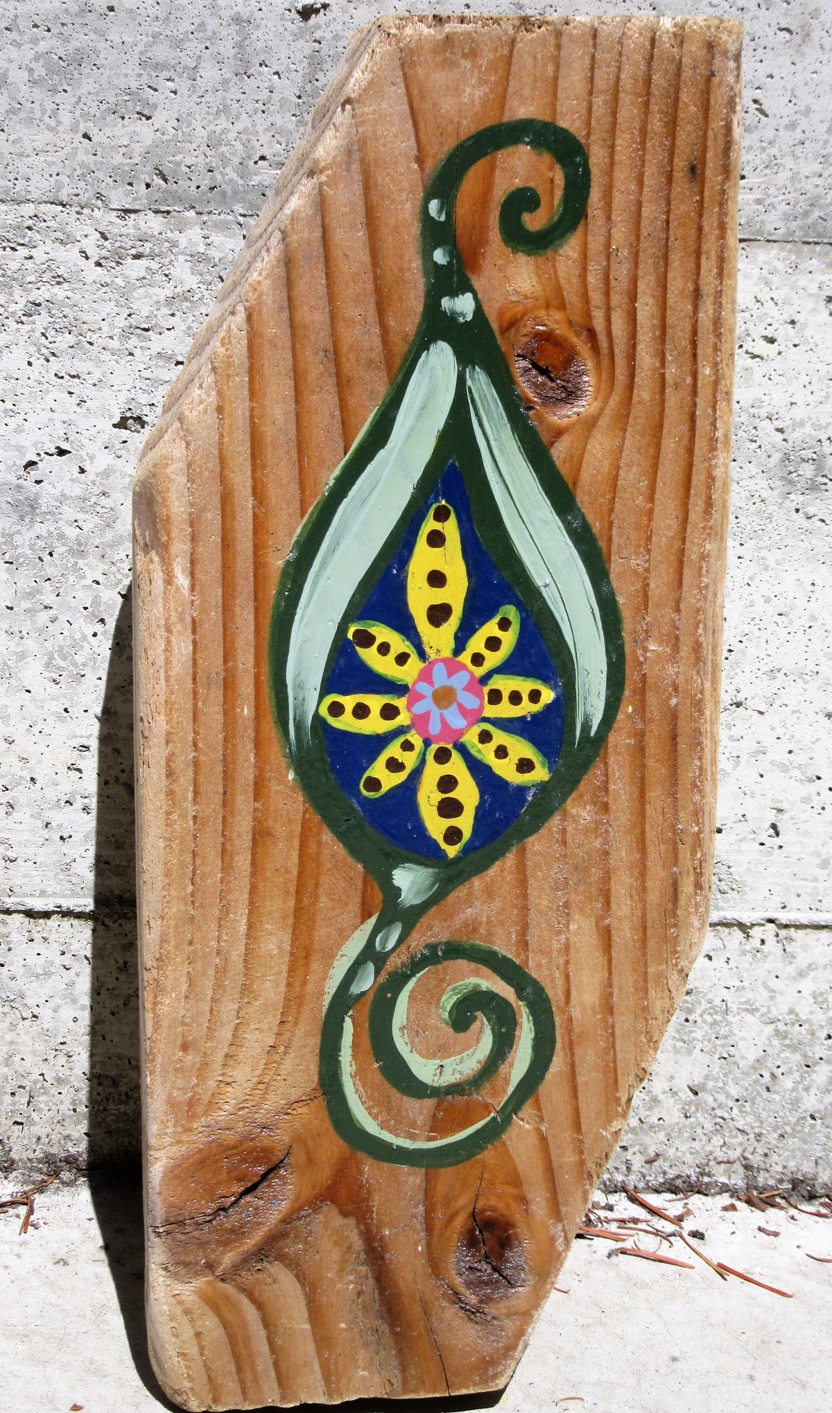 Folk art leaf motif painted on a wood plank by Lone Peep: a yellow dotted flower on blue inside a green leaf with a spiral.