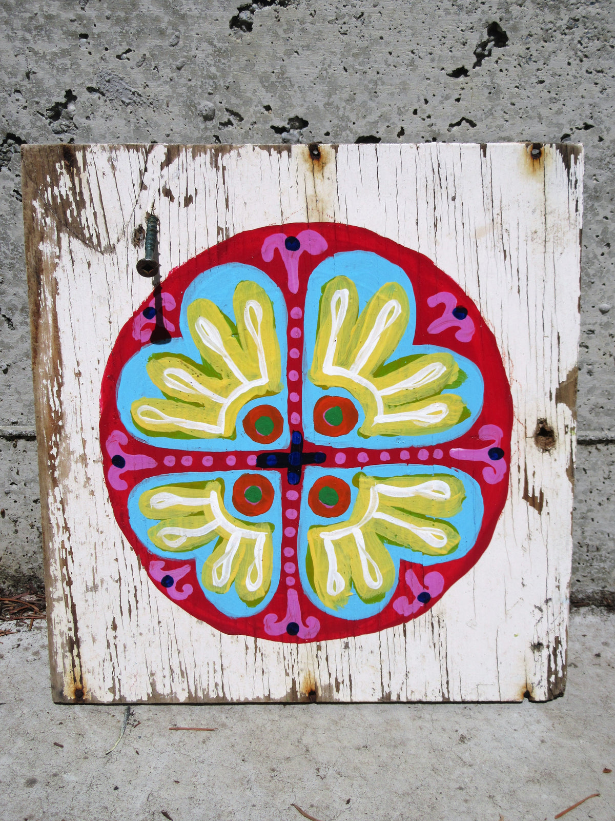 Folk art mandala painted on a whitewashed wood board by Lone Peep: red, blue, yellow and pink circular flower motif.