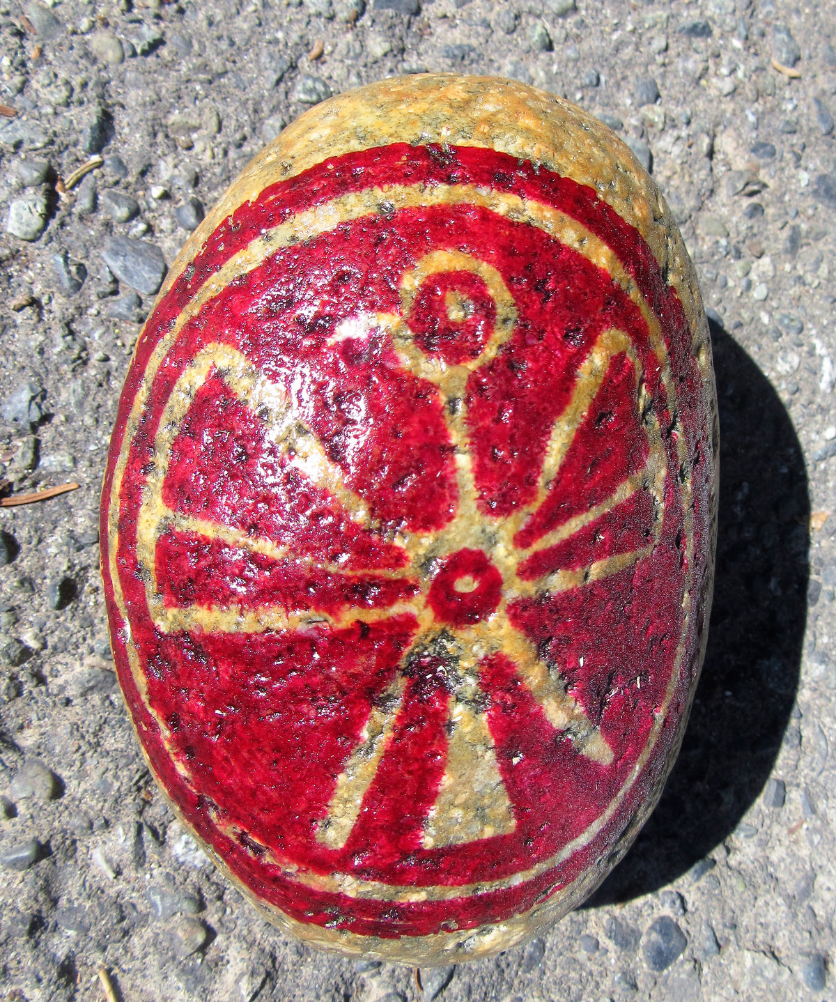 Painted stone by Lone Peep: deep red stone with a cream geometric star-and-swirl design.