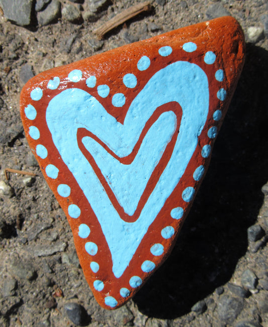 Painted stone by Lone Peep: terracotta stone with a light blue heart and dotted border.