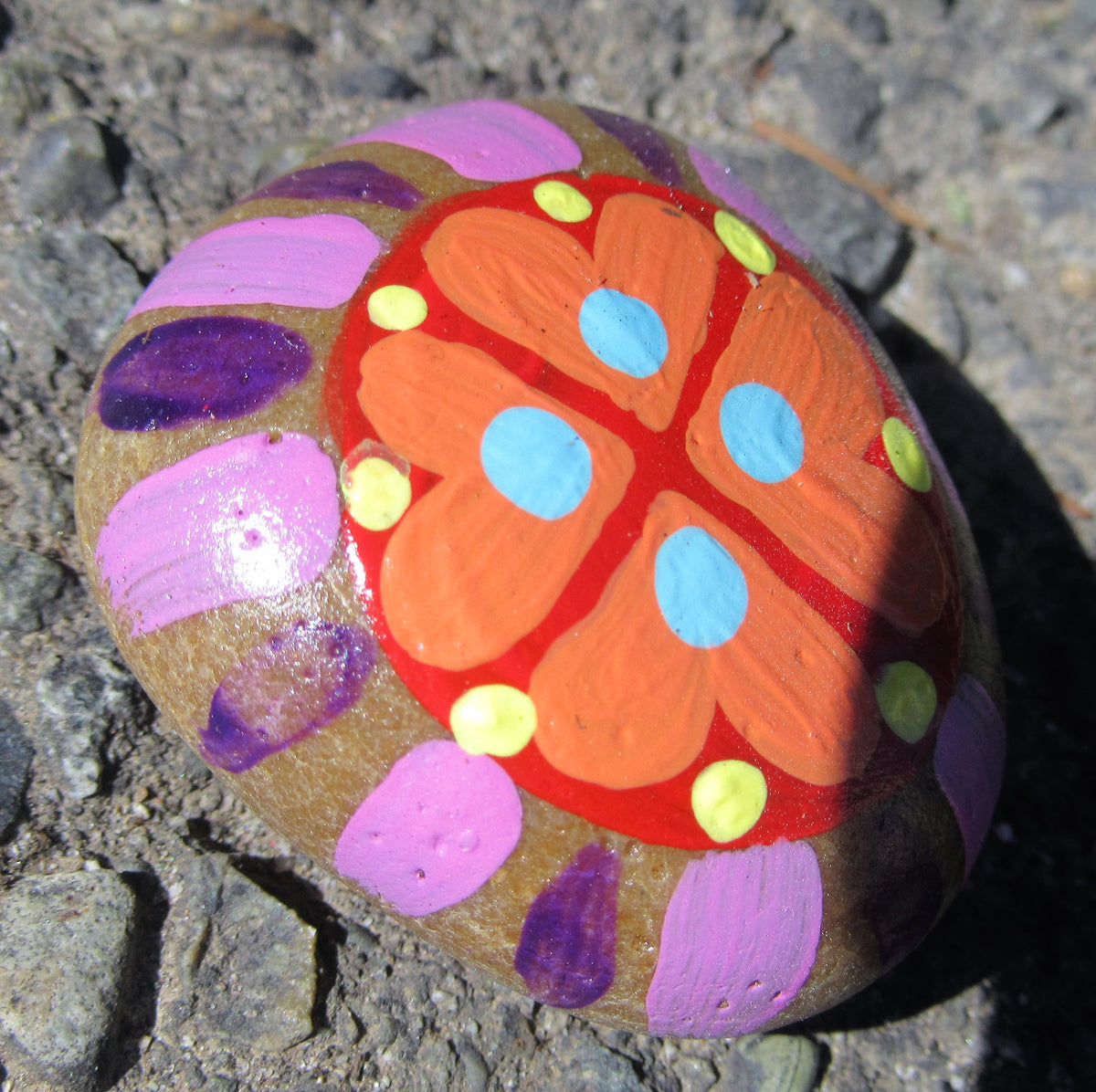 Painted stone by Lone Peep: round stone with an orange flower, blue dots and purple-pink petals.