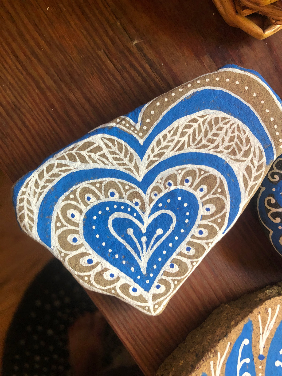 A heart-shaped decorative item with a blue and beige mandala pattern, resting on a dark wooden surface.
